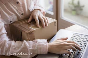 photo of lady holding box and typing on laptop 